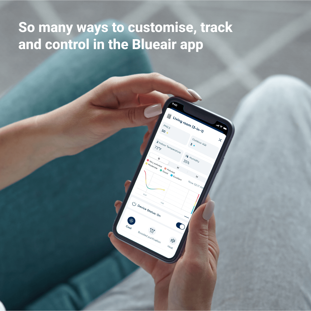 Person holding a smartphone with the Blueair app displayed, sitting on a couch.